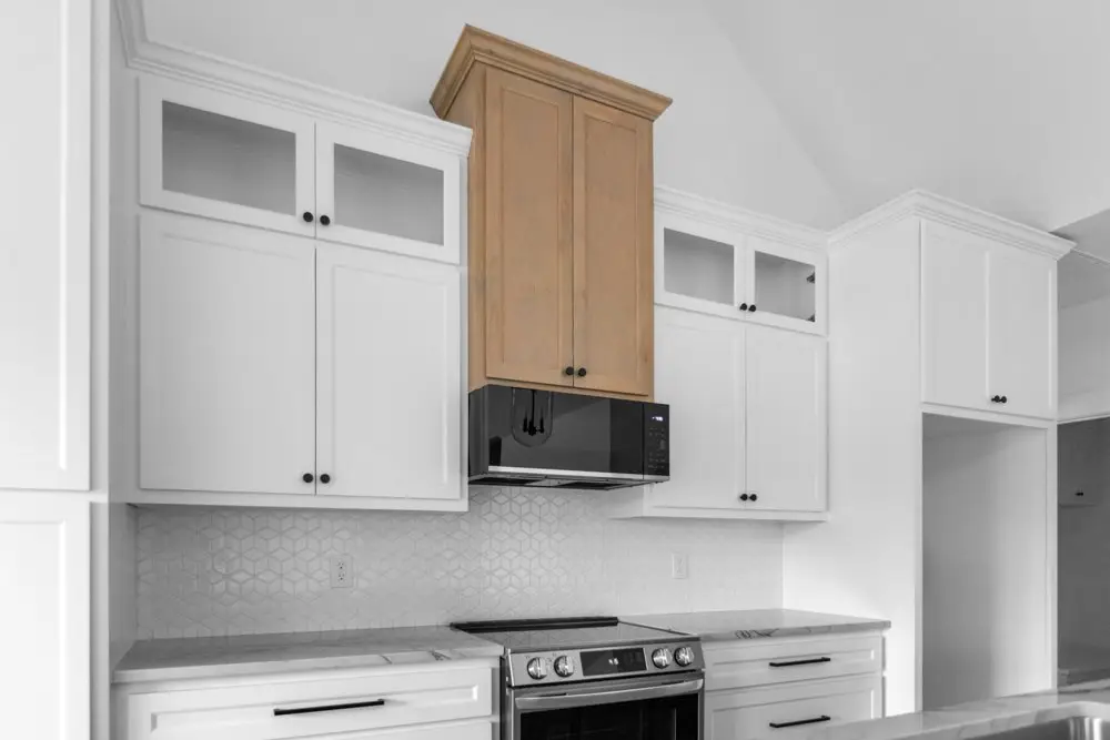 Kitchen in white cabinetry with a wood vent hood, The Dahl House, a custom home in Sherman, Texas