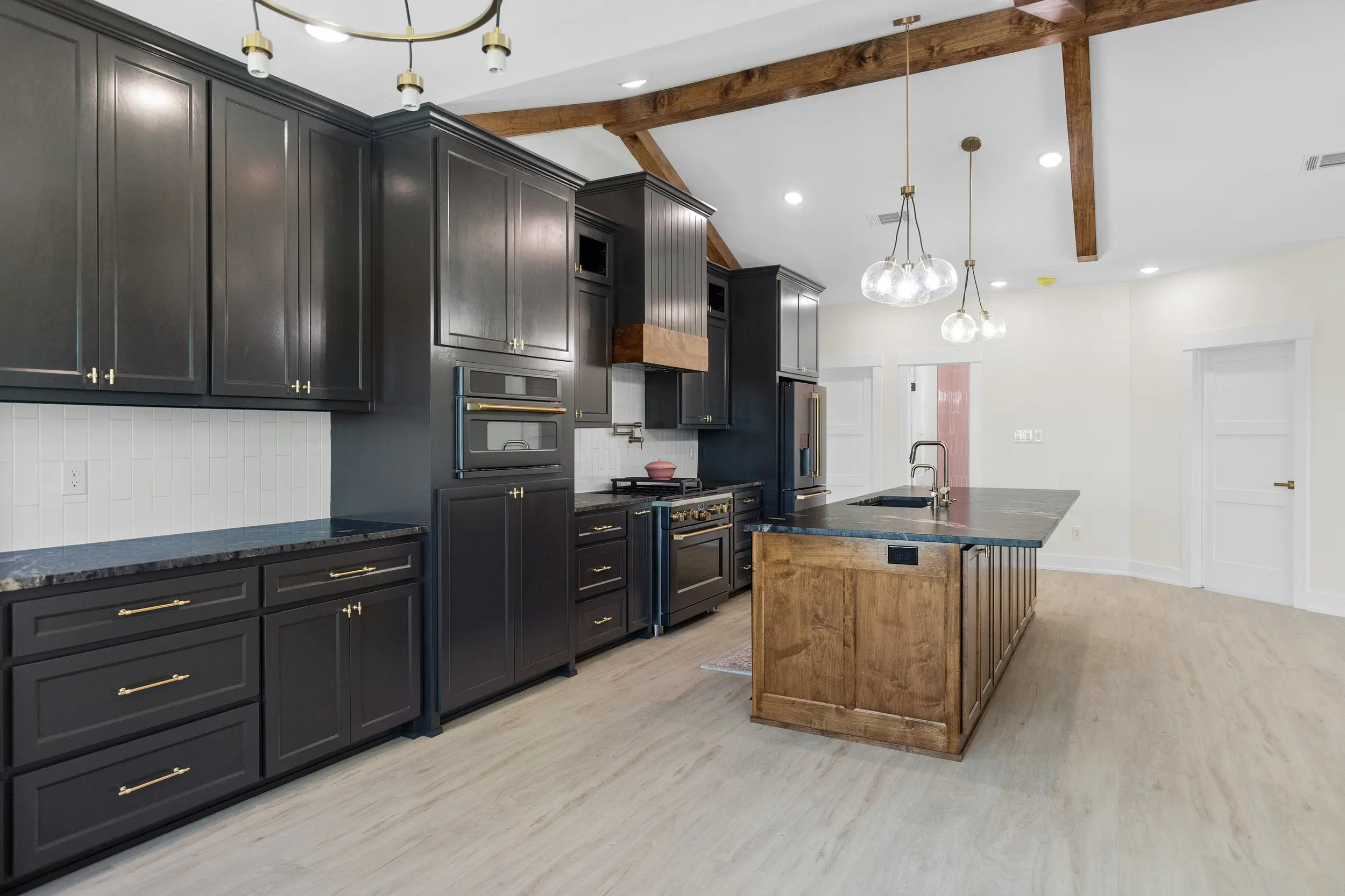Kitchen with dark cabinetry and a wood island under exposed beams, The Lugo House, a custom home in Sherman, Texas