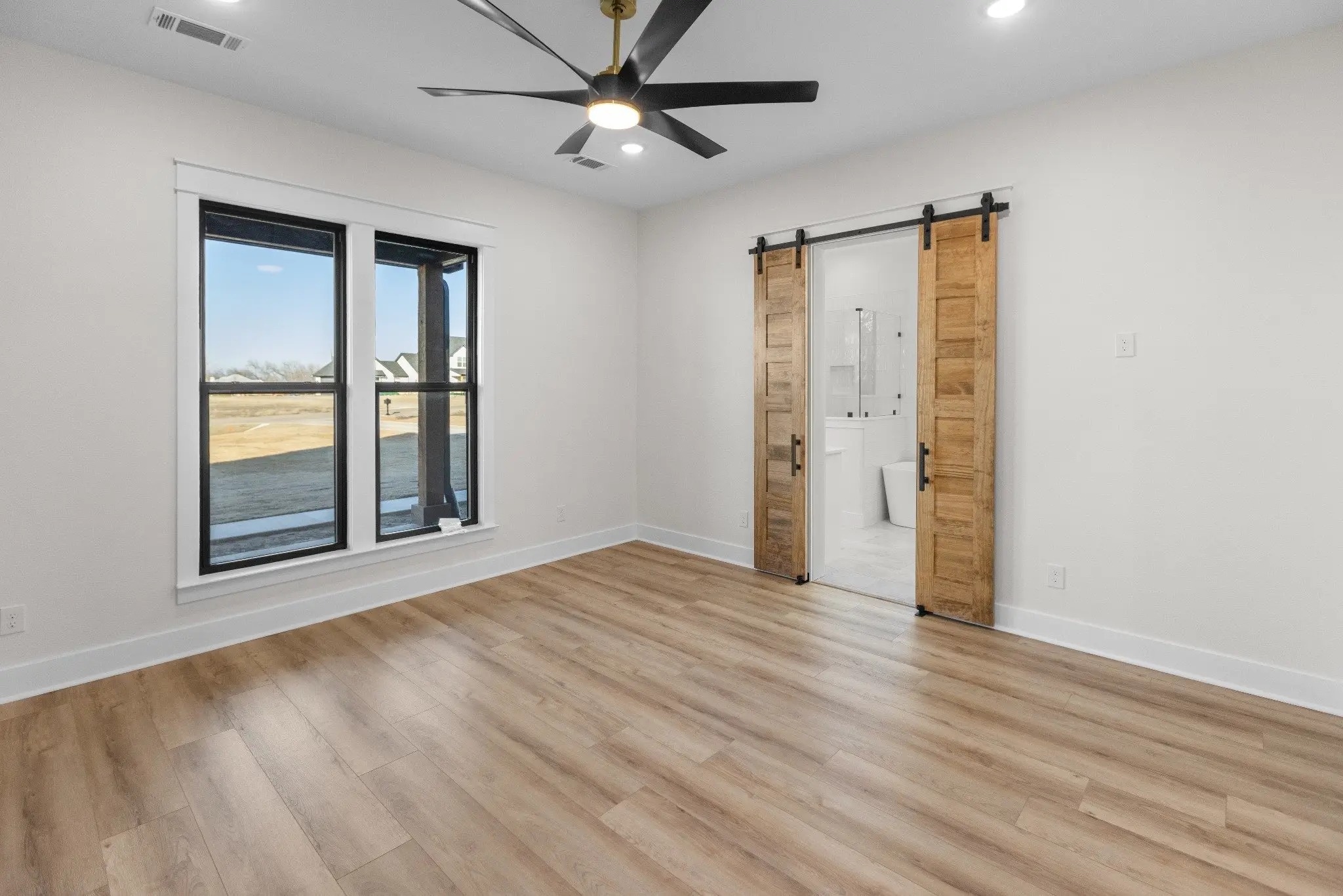 Bedroom with a sliding barn door and corner windows, The Wester House, a custom home in Sherman, Texas